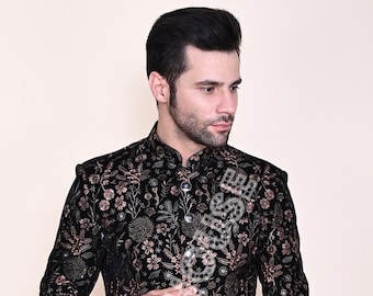 Könnte beinhalten: Eine schwarze Samtjacke mit langen Ärmeln und einem floralen Muster in Gold und Rosa. Die Jacke hat einen Stehkragen und einen Knopfverschluss.