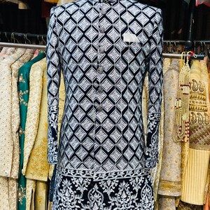 May include: A black and white patterned jacket with a mandarin collar and silver buttons. The jacket features a geometric design and ornate embroidery along the hem and cuffs. A white pocket square is visible.