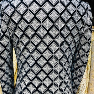 May include: A black and white patterned jacket with a geometric design. The jacket features a repeating diamond pattern with floral accents. The fabric appears to be velvet or a similar soft material. The jacket has long sleeves and a high collar.