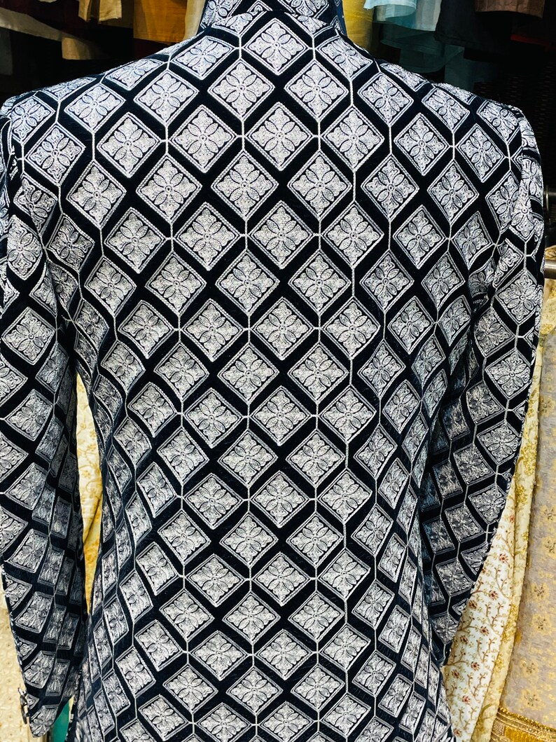 May include: A black and white patterned jacket with a geometric design. The jacket features a repeating diamond pattern with floral accents. The fabric appears to be velvet or a similar soft material. The jacket has long sleeves and a high collar.