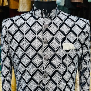 May include: A black and white patterned jacket with a high collar and ornate buttons. The jacket features a diamond pattern with floral accents and a pocket square. The mannequin's neck size is 40 inches.