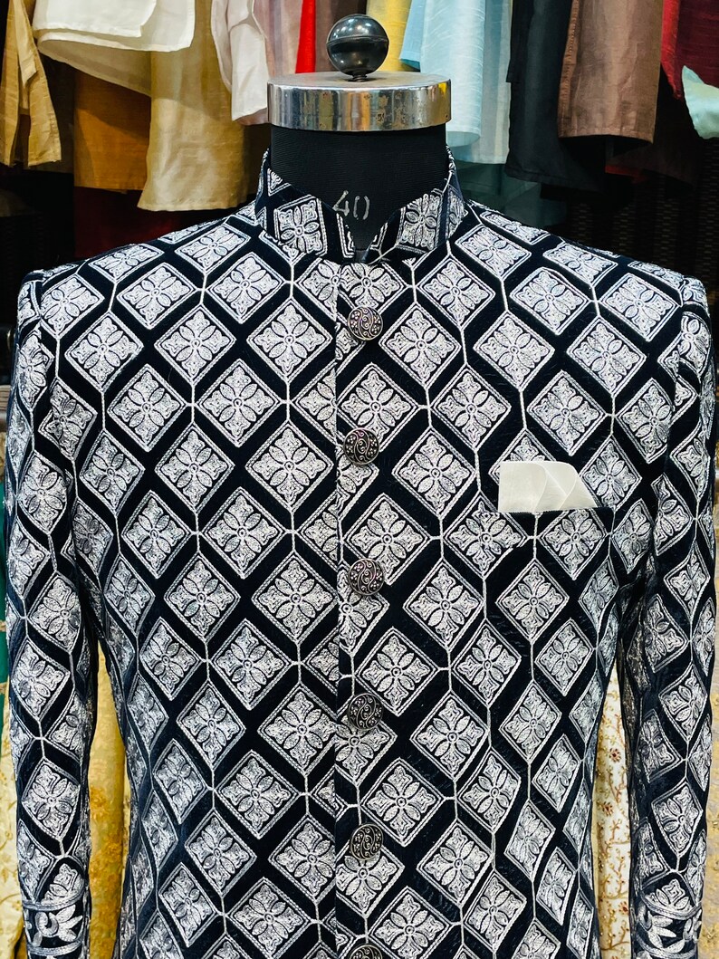 May include: A black and white patterned jacket with a high collar and ornate buttons. The jacket features a diamond pattern with floral accents and a pocket square. The mannequin's neck size is 40 inches.