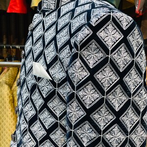 May include: A black velvet jacket with a diamond pattern embroidered in white. The jacket has a mandarin collar, decorative buttons, and a white pocket square. The pattern is a repeating geometric design with floral elements.