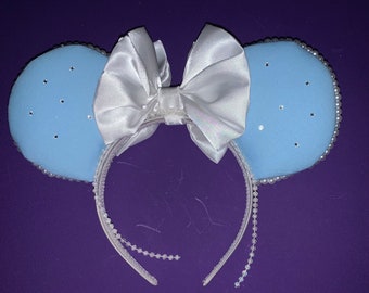 May include: Light blue mouse ears with a white satin bow and pearl accents.
