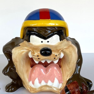 May include: A white ceramic mug with a black handle and the text "But first, coffee" in a black, handwritten-style font. The mug is on a white surface.