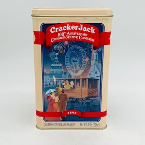 May include: A rectangular Cracker Jack 100th Anniversary commemorative canister. The tan metal tin features a red banner with the words "Cracker Jack" and "100th Anniversary Commemorative Canister". The bottom of the tin reads "CARAMEL POPCORN AND PEANUTS NET WT. 8 Oz. (226g)".