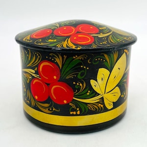 May include: A round, black wooden box with a lid, adorned with a vibrant floral design. The lid and sides feature red berries, green leaves, and yellow accents. A gold band encircles the base, adding a touch of elegance to this decorative storage item.