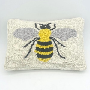 May include: A rectangular throw pillow with a textured, off-white hooked yarn surface. The center features a large, stylized bee motif with a bright yellow and black striped body, grey wings, and black legs, all created with a raised loop pile.