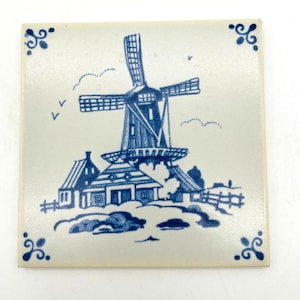 Peut inclure: Carreau de céramique carré avec un motif de moulin à vent bleu et blanc. La tuile présente une illustration détaillée d'un moulin à vent hollandais, de maisons et d'une clôture. Des accents floraux bleus décoratifs complètent le design. Une charmante pièce pour la décoration intérieure.