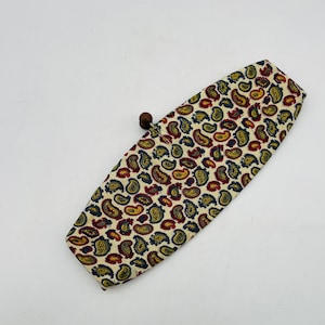 May include: A rectangular clutch with a cream-colored background and a paisley pattern in red, yellow, and navy blue. The clutch has a wooden ball clasp on one end. The paisley pattern is a classic design.