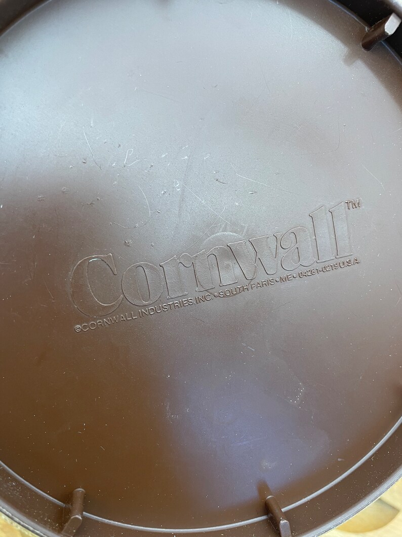 May include: A brown plastic lid with the embossed word "Cornwall" and the text "&copy;Cornwall Industries Inc. South Paris, ME 04281-0319 U.S.A." The lid has a slightly textured surface and is circular in shape.