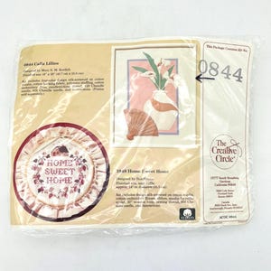 May include: A plastic-wrapped embroidery kit package featuring two designs: 0844 Calla Lillies with a finished size of 16 inches by 20 inches, and 1948 Home Sweet Home with a finished size of approximately 14 inches in diameter, including a ruffled edge.