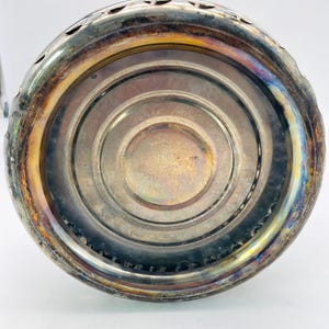 May include: A circular metal object with a tarnished silver-tone finish and a decorative scalloped edge. The centre features embossed text that reads "SIMPLEX PATENT" and "MADE IN ENGLAND," with concentric circular grooves surrounding the base.