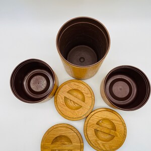 May include: A collection of three brown and tan plant pots with matching wooden lids. The pots are cylindrical with a textured exterior. The lids are round with a carved design. The interior of the pots is a dark brown colour.