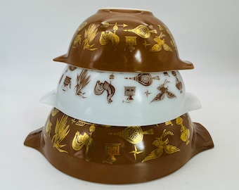 May include: A stack of three round glass mixing bowls with side handles. The top and bottom bowls are brown with gold metallic graphics, while the middle bowl is white with brown graphics. The pattern features roosters, corn, and kitchen tools.