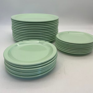 May include: A collection of light green plates stacked in three separate piles. The plates have a simple, rounded design and a smooth, glossy finish. The plates are a solid color and appear to be made of ceramic or a similar material.