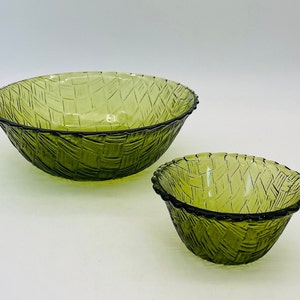 May include: Two green glass bowls with a woven basket design. The bowls are different sizes, with a larger bowl in the background and a smaller bowl in the foreground. The rims are dark green.