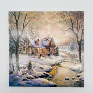 May include: A winter scene painting depicts a snow-covered cabin with a bridge over a stream. Bare trees frame the cabin, and the sky is a soft blend of colors. The cabin has lights on, suggesting a warm interior.