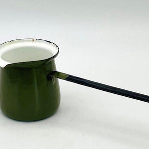 Op de afbeelding: Een olijfgroene emaille koffiepot met een witte binnenkant en een lange, dunne zwarte steel. De pot heeft een kleine schenktuit aan de rand en een gladde, glanzende afwerking. De constructie is eenvoudig, met een cilindrisch lichaam.