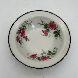 May include: A white ceramic bowl with a black rim and floral design. The bowl features a delicate pattern of pink flowers and green leaves. The bowl is round and has a slightly recessed center.