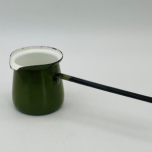 Op de afbeelding: Een groene emaille koffiepot met een lange zwarte handgreep. De pot heeft een wit interieur en een tuit om gemakkelijk te schenken. Deze pot in vintage-stijl is perfect voor het zetten van koffie of het verwarmen van vloeistoffen.