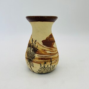 May include: A ceramic vase with a beige base and a dark brown rim. The vase features brown swirled patterns and black plant illustrations. The vase has a wide base and a narrow neck.
