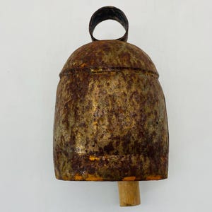 May include: A rustic metal bell with a weathered, textured surface. The bell has a dark brown, gold, and rust colour scheme. It features a loop at the top for hanging and a wooden clapper. This decorative bell is suitable for home decor.
