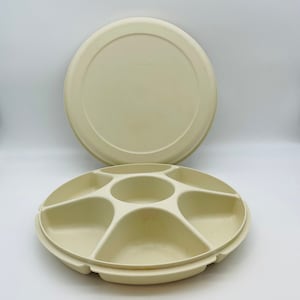 May include: A vintage beige plastic serving tray with a lid. The tray is divided into seven sections, with a central circular compartment and six surrounding wedge-shaped compartments. The lid is round and flat.