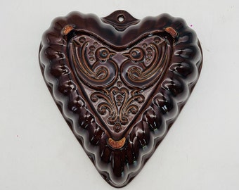 May include: A brown ceramic heart-shaped mold with a raised design of two birds and floral accents. The mold has a scalloped edge and a hanging loop.