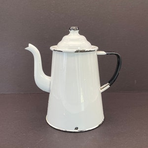 May include: White enamel coffee pot with a black handle and trim. The pot has a lid with a black knob and a spout for pouring. The pot has a classic, vintage design.