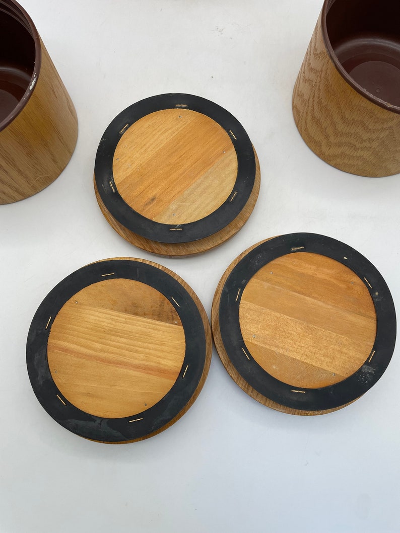 May include: Wooden coasters with a dark brown rubber ring and a light brown wooden centre. The coasters are round and have a natural wood grain pattern. Several wooden containers with a brown interior are also visible.