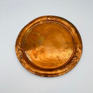 May include: A round copper serving tray with a hammered finish and a decorative floral design around the rim.