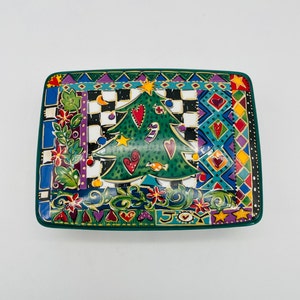 May include: A green ceramic serving tray with a colorful Christmas tree design. The tree is decorated with hearts, candy canes, and stars. The tray has a green border and a white background with a checkered pattern. The words "Joy" are written on the bottom of the tray.
