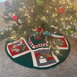 May include: A decorated Christmas tree with red and green ornaments and lights. A green tree skirt with red and white patchwork designs is at the base of the tree. A small blue truck ornament is visible.