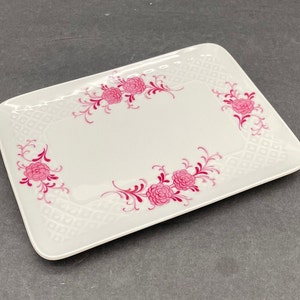 May include: A rectangular white ceramic tray featuring a subtle embossed diamond grid pattern across the surface and a decorative border of bright pink floral motifs with swirling vine accents positioned at the corners and sides.