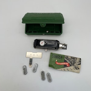 May include: An open, dark green Singer sewing machine case with a black buttonholer and various metal attachments. A Singer Buttonholer instruction booklet is also present.