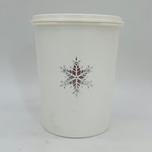 May include: A white plastic tumbler with a matching lid. A silver snowflake design is centered on the front. The tumbler is cylindrical and appears to be empty. The background is plain white.