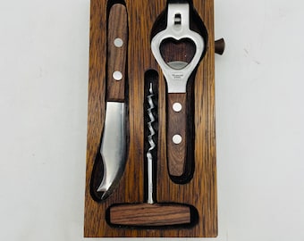 Op de afbeelding: Een houten doos met een flessenopener, een kurkentrekker en een mes. De gereedschappen zijn van metaal en hebben houten handvatten.