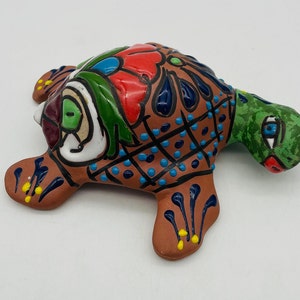 May include: Hand-painted ceramic turtle figurine with colourful details, including green, blue, red, and yellow accents. The turtle is in a walking position with its head turned to the side.