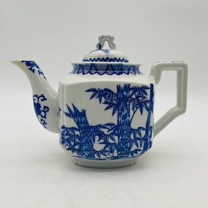 May include: A white teapot with a blue and white bamboo design. The teapot has a lid with a knob on top. The teapot is on a white background.