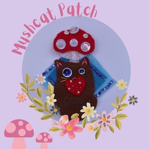 May include: A whimsical felt patch featuring a brown cat with a red heart, a red mushroom, and the text "Myshcat Patch". The patch is decorated with beads and sequins, surrounded by floral and mushroom illustrations on a lavender background.