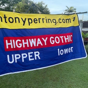 Puede incluir: Una pancarta azul y amarilla con el texto "antonyperring.com" y "HIGHWAY GOTHIC" en blanco. La pancarta también tiene las palabras "UPPER" y "lower" en blanco.