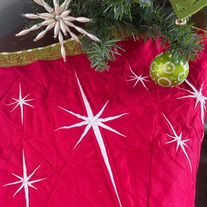 Puede incluir: Falda de árbol de Navidad acolchada roja con diseños de estrellas blancas. La falda tiene un ribete verde y dorado.