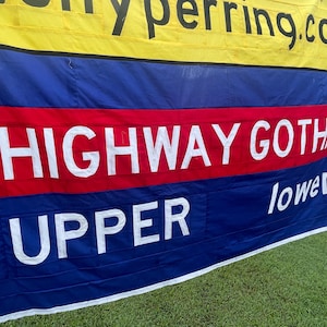 Op de afbeelding: Een blauwe en rode banner met de tekst "HIGHWAY GOTHIC" in witte letters. De banner heeft ook de woorden "UPPER" en "lower" in witte letters.