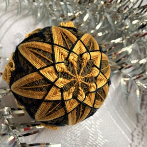 Puede incluir: Un adorno de color marrón dorado y azul marino cosido a mano con un patrón de estrella. El adorno está hecho de hilo y es una artesanía japonesa tradicional.