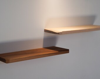 May include: Two wooden floating shelves mounted on a white wall. The lower shelf is a dark brown, while the upper shelf is a lighter tan color. Both shelves have a beveled edge.