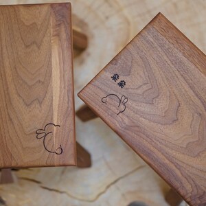 May include: Two wooden stools with a bunny rabbit design and the text "茶 茶" engraved on the top. The stools are made of light brown wood and have a natural finish.