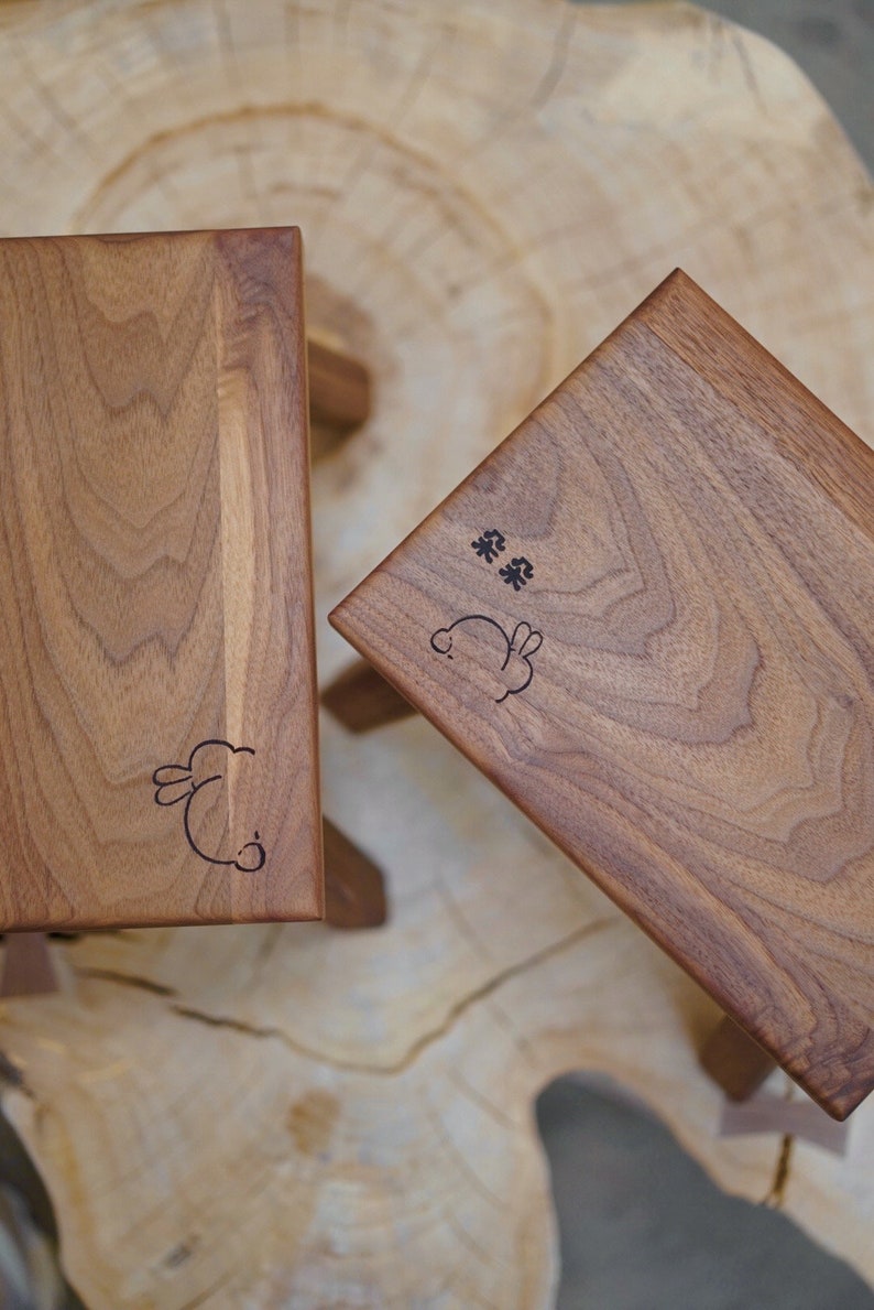 May include: Two wooden stools with a bunny rabbit design and the text "茶 茶" engraved on the top. The stools are made of light brown wood and have a natural finish.