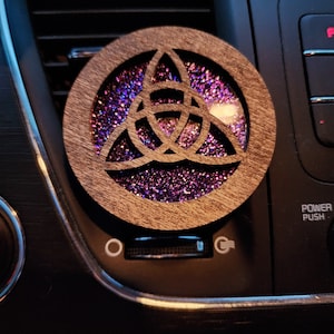 May include: A wooden car air freshener with a purple and blue glitter design inside. The design is a Celtic knot, also known as a triquetra or trinity knot.