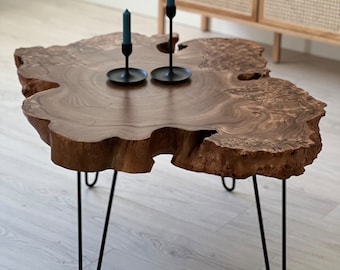 May include: A wooden coffee table with a natural, irregular shape and a dark brown finish. The table has four black hairpin legs and is decorated with two black candle holders with blue candles.